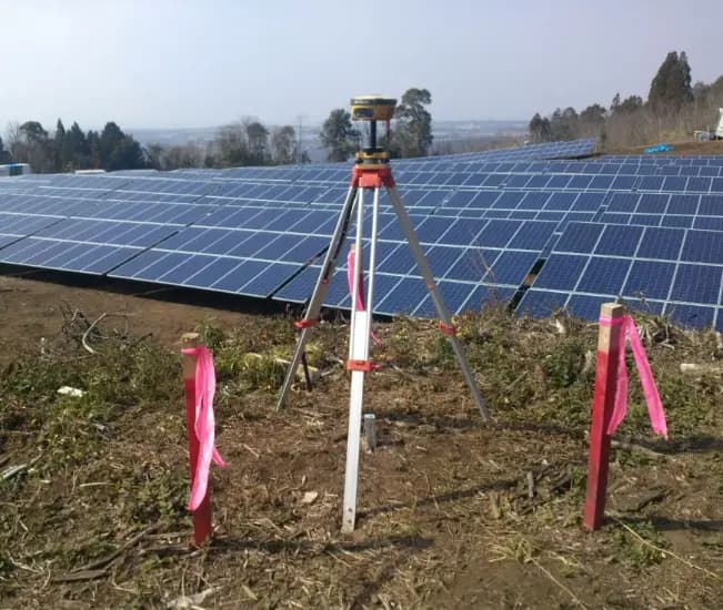 Equipo topográfico GNSS en terreno junto a una planta fotovoltaica